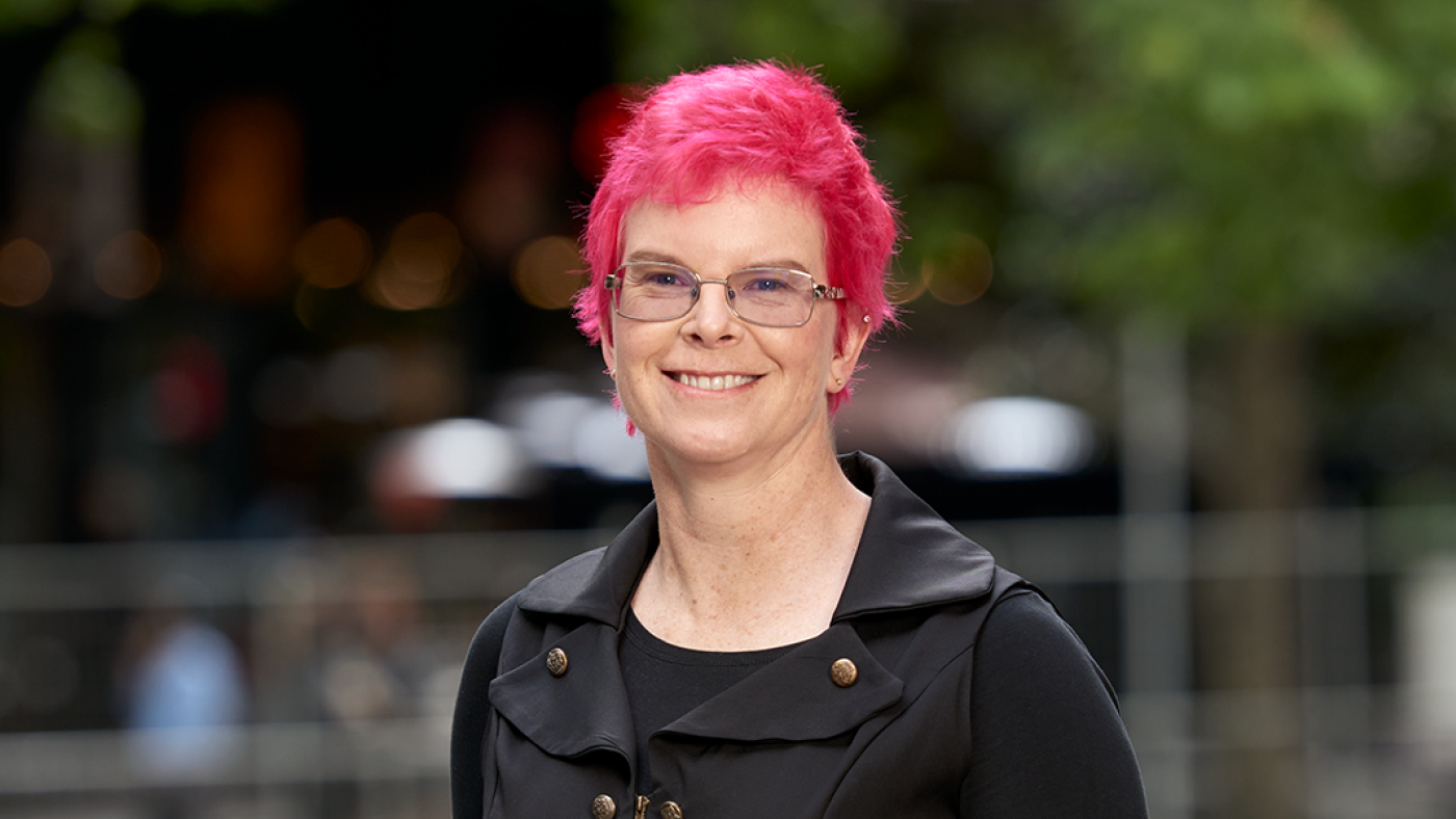 Fastmail chief of staff Nicola Nye in glasses wearing a black buttoned jacket with blue jeans.